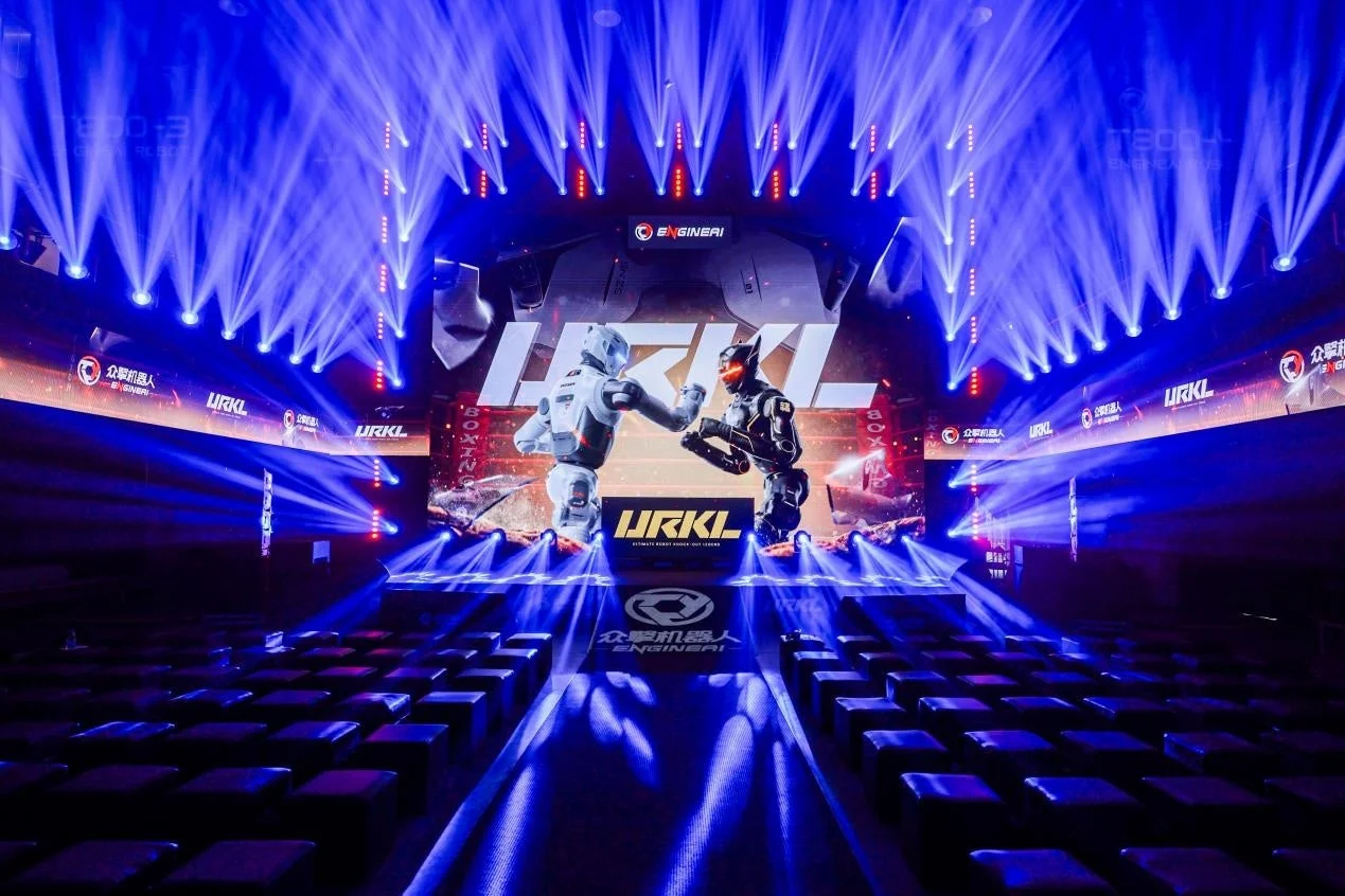 青いスポットライトが輝くステージで、2体のロボットが格闘する様子